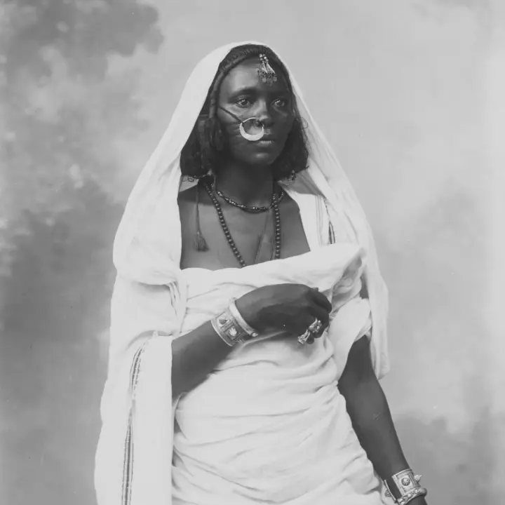Retrato de una mujer africana vestida con traje tradicional y luciendo joyas decorativas.